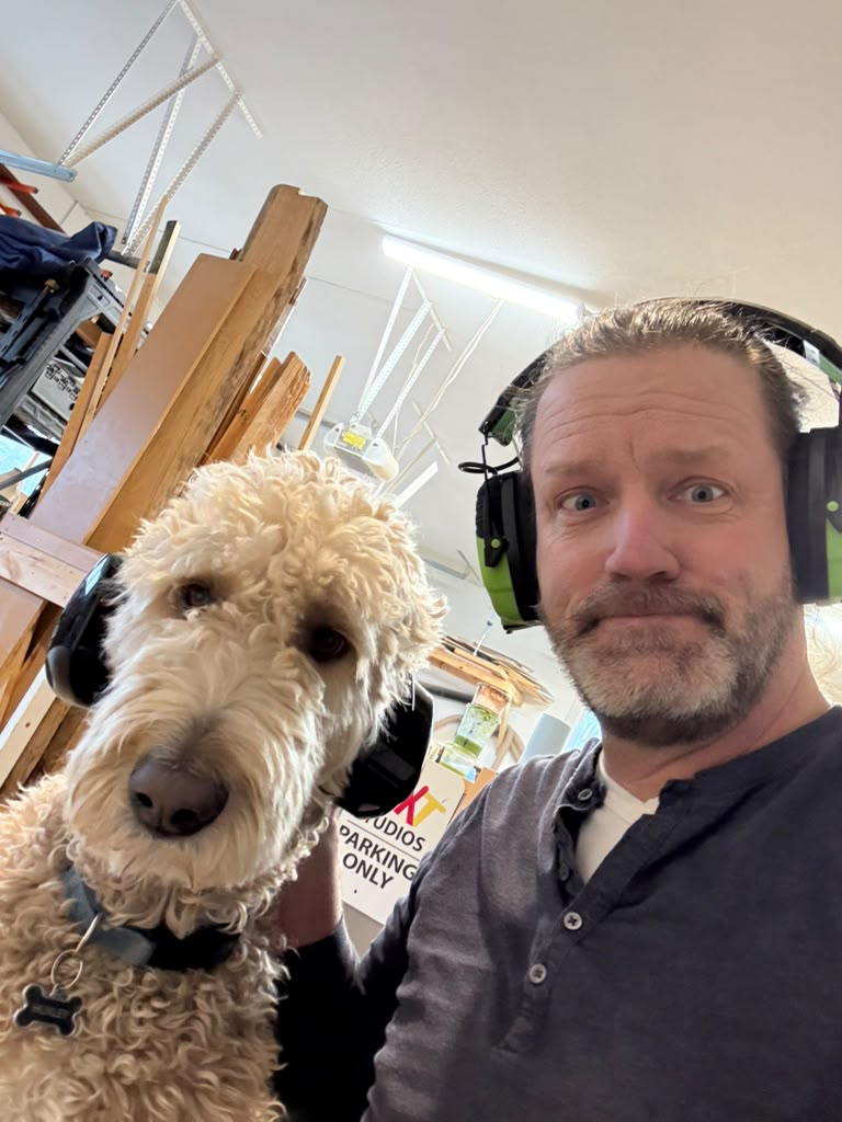 Mark Alan Sandberg and his studio dog Huxley wearing matching ear protection in the workshop