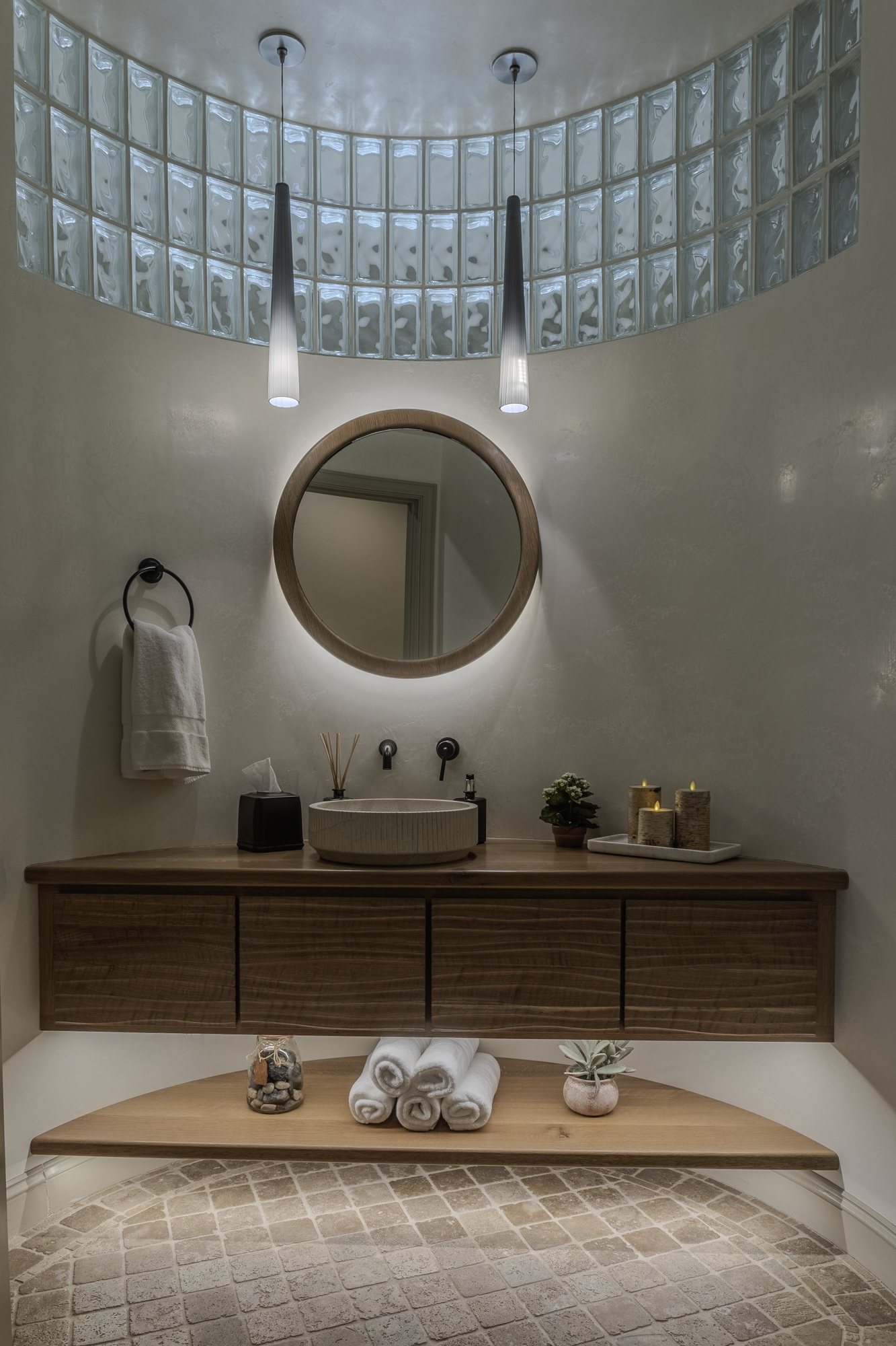 A tailored round powder room vanity with a stone top and integrated lighting